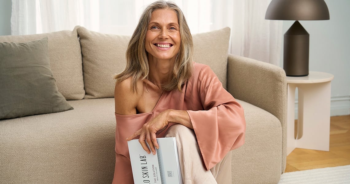 Woman sitting in front of couch holding a The Solution collagen package